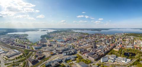 Tampereen keskusta-alueen ilmakuva, jossa on rakennuksia järviä ja viheralueita. Kuva on otettu kesällä aurinkoisella säällä.
