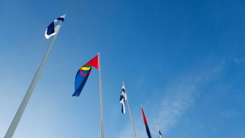 Viisi lippua liehumassa lipputangoissa. Suomen lippu ja saamelaisten lippu.