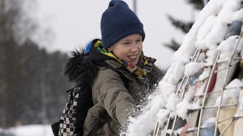 Lapsi kiipeämässä lumisen telineen reunalla.