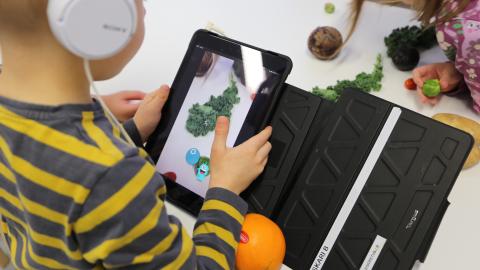 Esikouluikäinen lapsi kuvaa kasviksia tabletin kameralla ja tunnistaa niitä Vegemi-sovelluksen avulla.