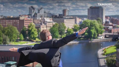 A person spreads their arms like the wings of an aeroplane. Tampere cityscape in the background. 