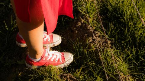 Henkilöstä, jolla on päällään punainen hame ja kengät ja joka seisoo nurmikolla, näkyy vain jalat.
