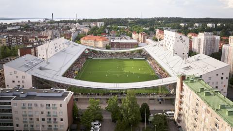 Tammelan Stadion kuvatuna ilmasta käsin niin että näkyy pelikenttä asuinkerrostalojen keskellä ja kuvassa korostuu stadionin muoto sekä kaarevat päätyrakenteet.