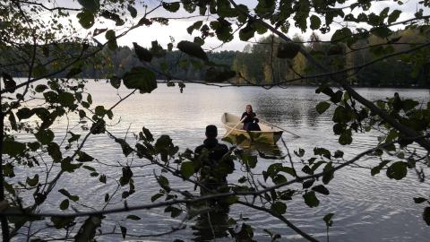 The photographer stands in the water and the rower rows.