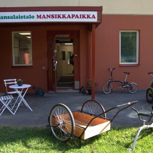 Erilaisia pyöriä ja maitokärryt Kansalaistalo Mansikkapaikan aurinkoisella etupihalla.