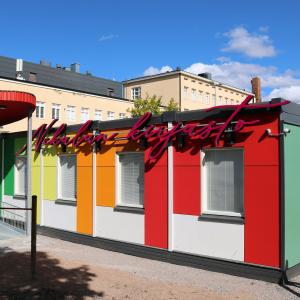 A colourful library made of Nekala containers and the oval canopy in front of it. The Nekala school building can be seen in the background. 