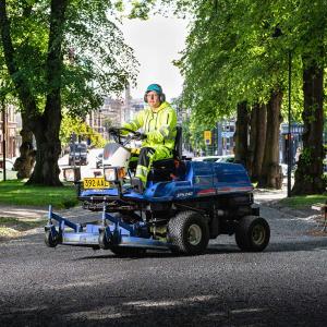 A maintenance worker driving a lawnmower on a park walkway.