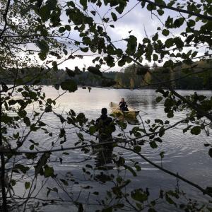 The photographer stands in the water and the rower rows.