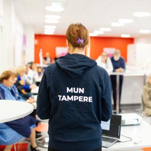 A city employee wearing a Mun Tampere hoodie is in front of the audience talking to them.