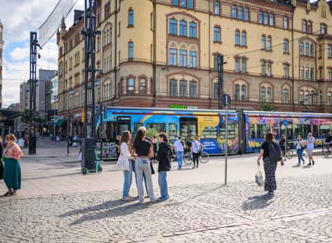 People standing and walking in the square, with a tram in the background.