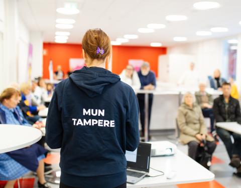 Mun Tampere -huppariin pukeutunut kaupungin työntekijä on yleisön edessä keskustelemassa heidän kanssaan.