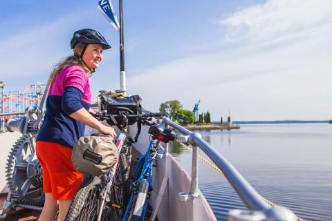 Pyöräilijä seisoo laivan kyydissä, taustalla näkyy Särkänniemi ja Näsijärvi. 