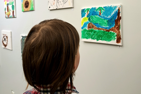 The child looks at the animal-themed artworks made by the children hanging on the wall.